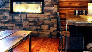 A stone fireplace with a glass viewing window, wooden flooring, and a rustic wooden wall.