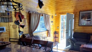 Interior acogedor de una cabaña con detalles de madera, un comedor con mesa y sillas, un sofá y una puerta que da al exterior.