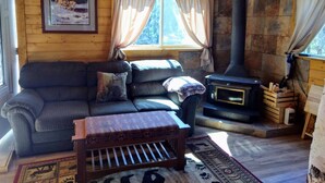 Interior acogedor de una cabaña con un sofá, un pequeño banco de madera, una chimenea y un cuadro en la pared.