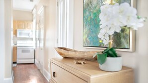 A hallway with a wooden dresser, a white vase with a white flower, and a painting on the wall. - Quaint Studio w/ Courtyard, 4 Blocks from River Street by Lucky Savannah (Savannah)