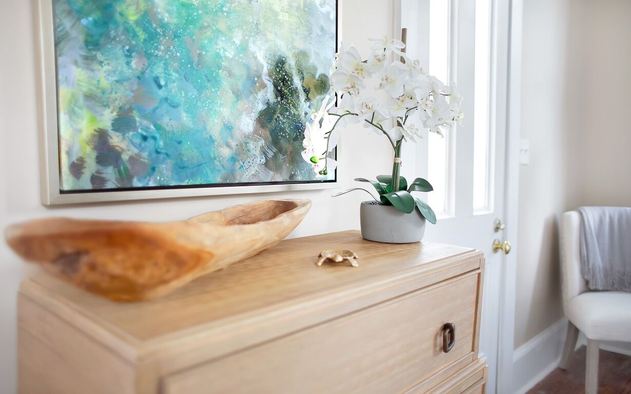 Un armari de fusta amb un quadre abstracte gran, una orquídia en test i un bol decoratiu.