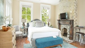 A bedroom with a bed, a dresser, a chair, a small table, a television, and a fireplace. - Quaint Studio w/ Courtyard, 4 Blocks from River Street by Lucky Savannah (Savannah)