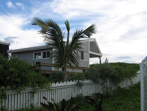 Une maison avec une clôture blanche en bois, un palmier et un ciel dégagé.
