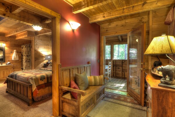 A cozy log cabin bedroom with a wooden bed, a bench with pillows, a dresser, and a lamp. - Peaceful Woods #25- Charming & Clean Log Cabin! (Sevierville)