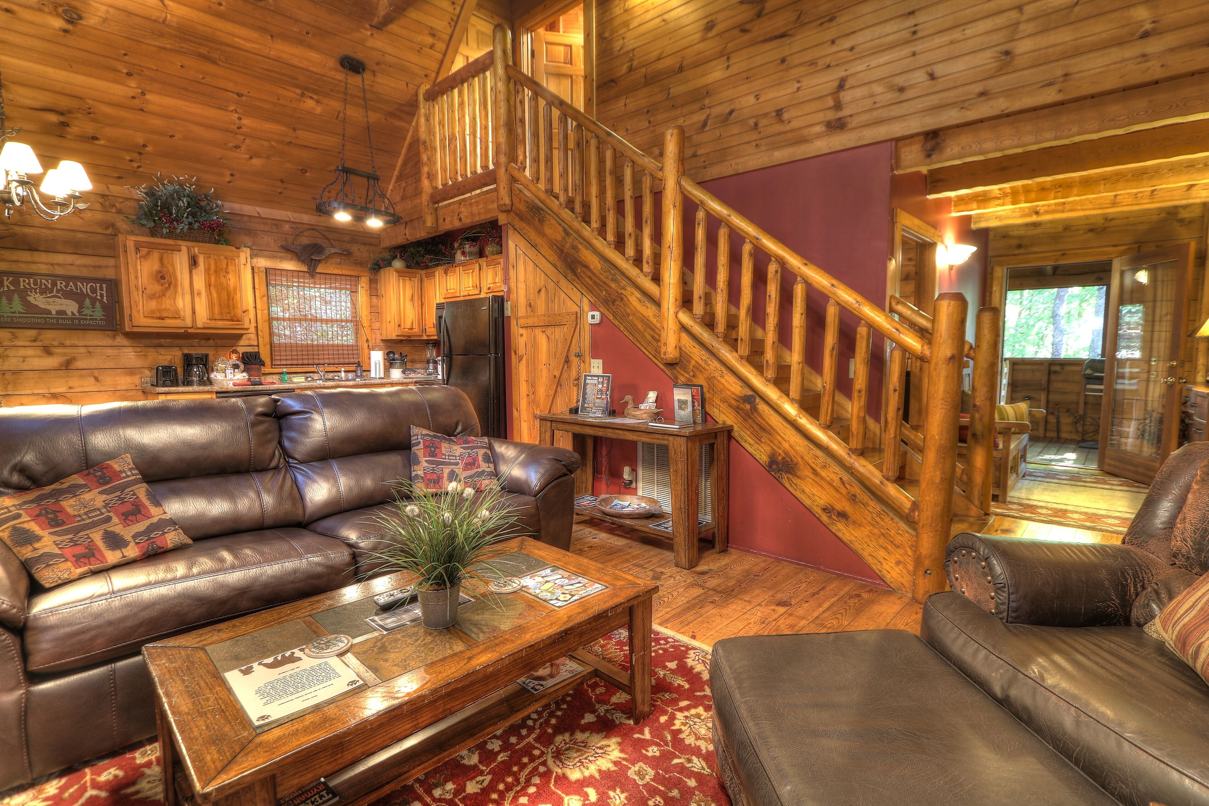 Un intérieur de chalet chaleureux avec un escalier en bois, des canapés en cuir, un coin repas et une cuisine.