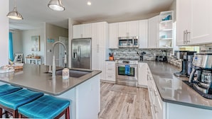 A modern kitchen with white cabinets, stainless steel appliances, and a central island with bar stools. - Steps From The Oceanfront! Pool, Pet Friendly, Wifi, king beds! WEEKLY DISCOUNTS (Cape San Blas)