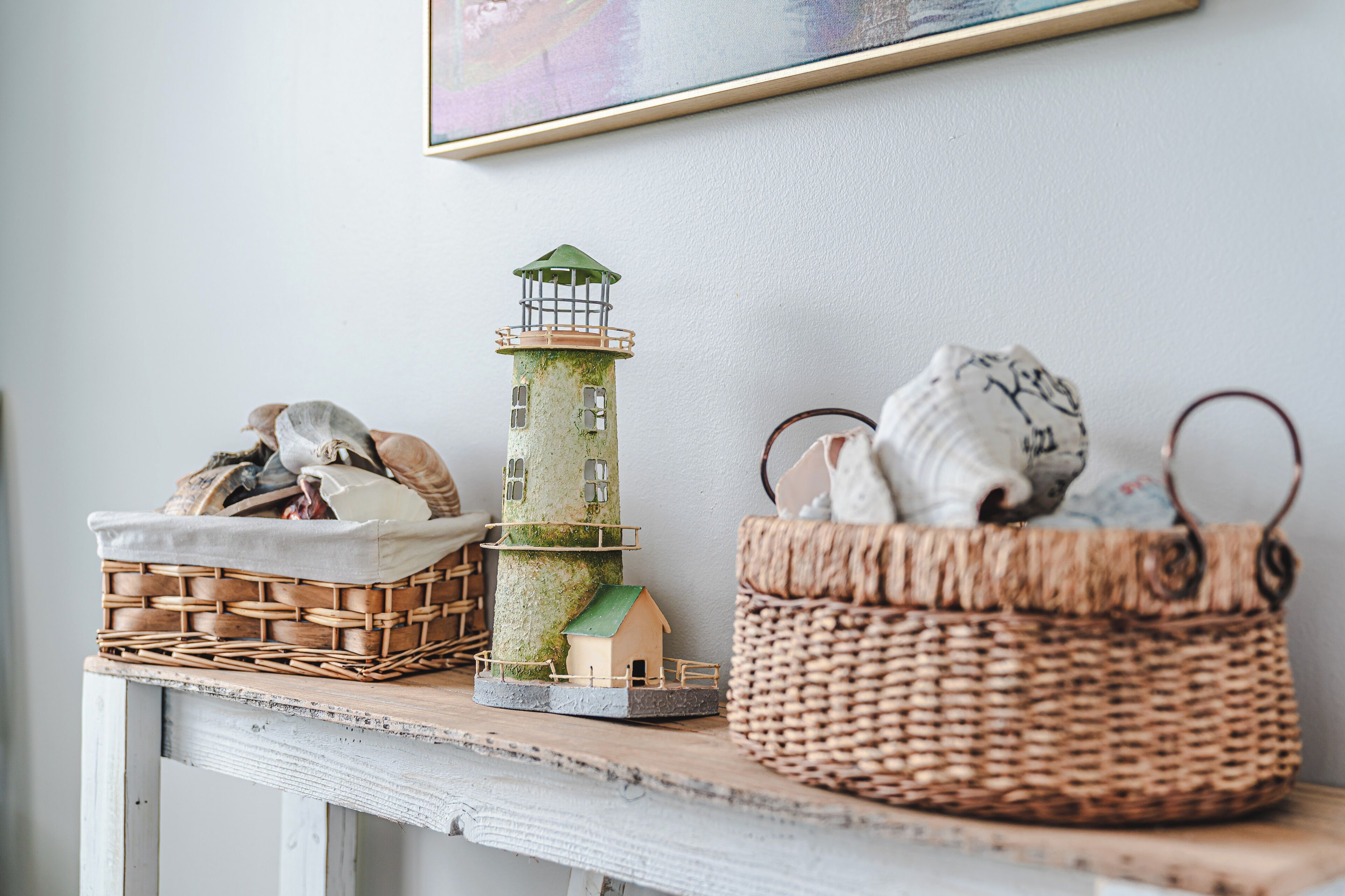 Une petite maquette de phare posée sur une étagère, un panier en osier contenant des sacs, et un tableau encadré accroché au mur.