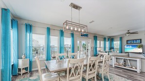 A dining area with a wooden table and chairs, a ceiling fan, and a television on a stand. - Steps From The Oceanfront! Pool, Pet Friendly, Wifi, king beds! WEEKLY DISCOUNTS (Cape San Blas)