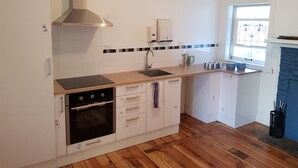 Uma cozinha moderna com armários brancos, forno preto, exaustor de aço inoxidável, pia e janela com grade decorativa.