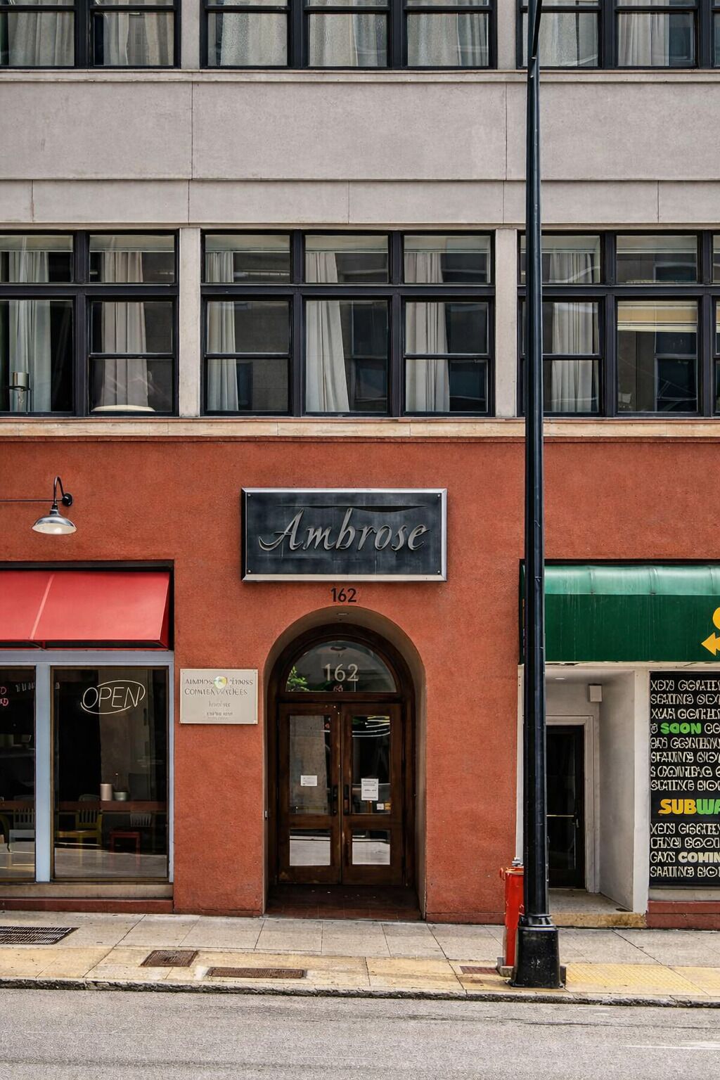 Un edificio con un letrero que dice "Ambrose" sobre la entrada, un toldo rojo y el número "162" sobre la puerta.