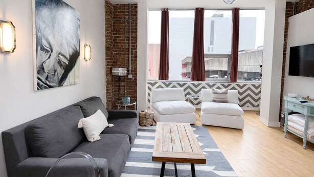 Een moderne woonkamer met een grijze bank, witte fauteuils, een houten salontafel en een groot schilderij aan de muur.