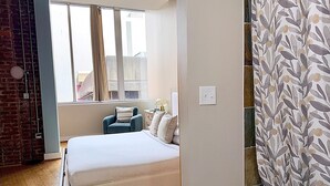 Een slaapkamer met een bed, een stoel, een raam en een gordijn.