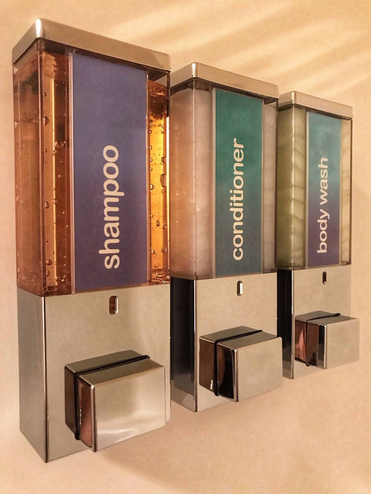 A wall-mounted dispenser with three compartments labeled 'shampoo,' 'conditioner,' and 'body wash.'