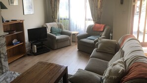 A living room with a sofa, armchairs, a TV, and a wooden coffee table.