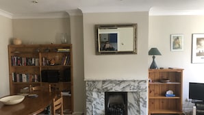 A living room with a fireplace, a wooden bookshelf, a dining table with chairs, and a television.