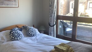 A bedroom with a bed, pillows, a bedside lamp, a window with curtains, and a view of the outside.