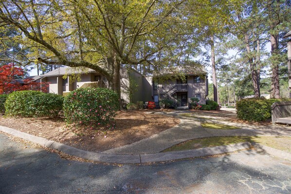 A residential area with two houses, one with a porch and a staircase, surrounded by trees and a driveway.