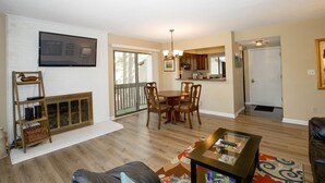 A living room with a fireplace, a dining area with wooden chairs, and a kitchen visible through an open door.