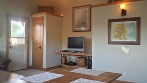 A living room with a wooden table, a television, and framed artwork on the wall. - Award Winning Cow Creek Suite: Edge-Of-Town Quiet & Convenience With Great Views (Ridgway)