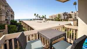 Ein Balkon mit Korbmöbeln, der Blick auf einen Strand und angrenzende Gebäude freigibt.