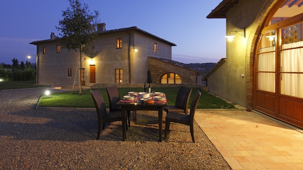 A dining area with a table set for four, surrounded by chairs, in front of a house with a stone facade and a wooden door. - Luxury Villa: Air-Co & Swimmingpool in Chianti/Sleeps 21 or more in extra suites (Montespertoli)