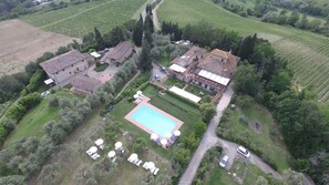 An aerial view of a property with a swimming pool, multiple buildings, and surrounding vineyards.