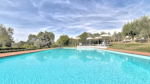 A rectangular swimming pool with clear blue water, surrounded by a wooden fence, and shaded by umbrellas. - Luxury Villa: Air-Co & Swimmingpool in Chianti/Sleeps 21 or more in extra suites (Montespertoli)