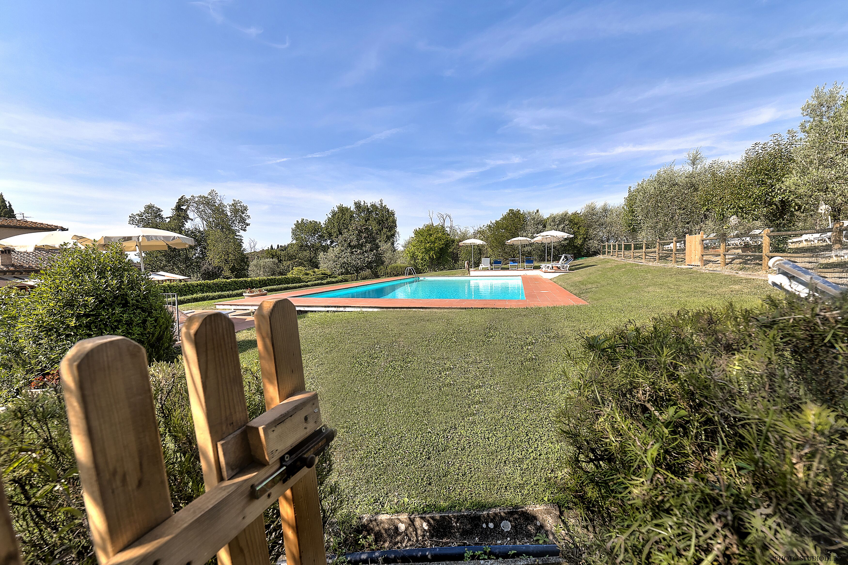 A swimming pool surrounded by a well-maintained lawn, with a wooden deck in the foreground.