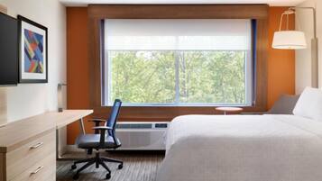 A hotel room with a large bed, a desk with a chair, a small table, and a window with a view of trees.
