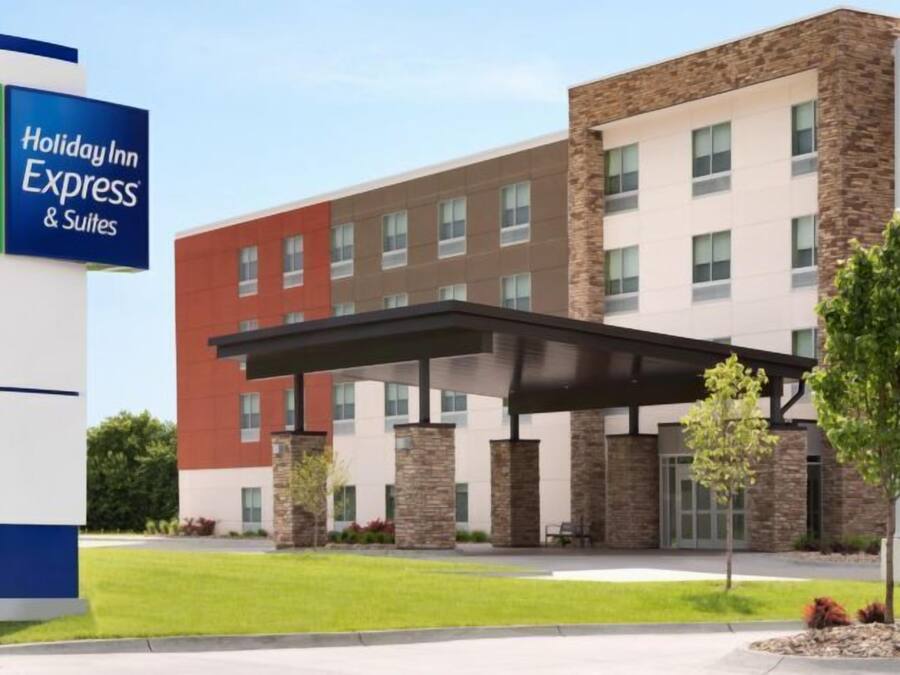 Um hotel Holiday Inn Express & Suites com design moderno, apresentando uma grande placa, entrada coberta e um jardim frontal ajardinado.