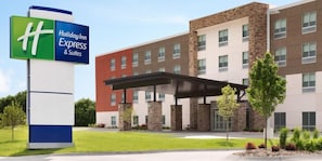 Ein Holiday Inn Express & Suites Hotel mit modernem Design, das ein großes Schild, einen überdachten Eingang und einen begrünten Vorgarten zeigt.