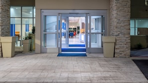 L’entrée d’un hôtel, avec une porte en verre, des piliers en pierre et un tapis bleu qui mène à l’intérieur.