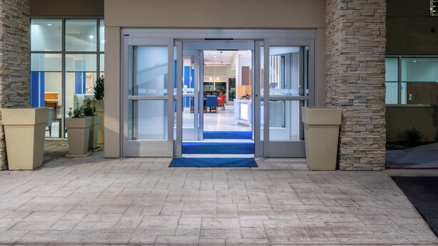 L’entrée d’un hôtel, avec une porte en verre, des piliers en pierre et un tapis bleu qui mène à l’intérieur.