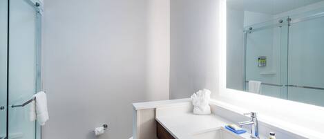 A modern bathroom with a glass shower enclosure, a white sink with a mirror, and a towel rack.