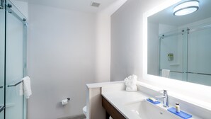 Une salle de bain moderne avec une douche à parois de verre, un lavabo blanc avec un miroir et un meuble-lavabo en bois.