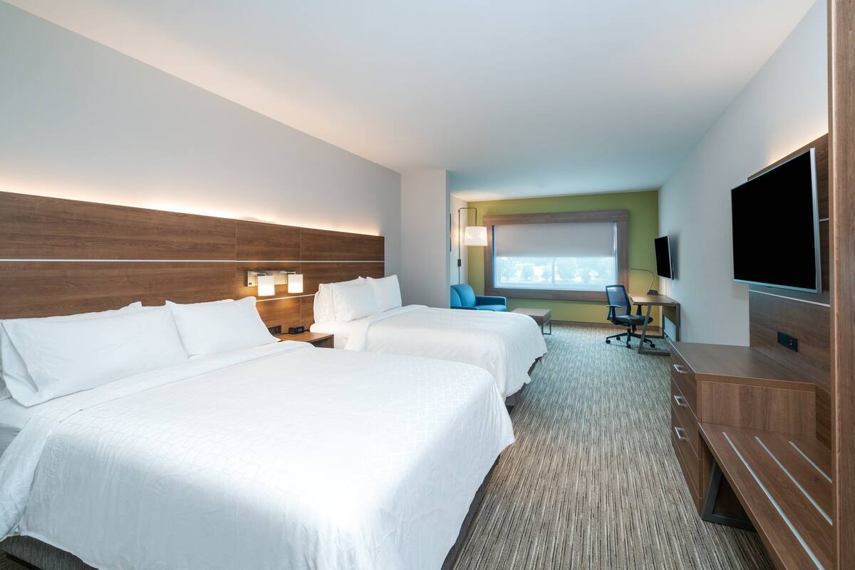 Une chambre d’hôtel avec deux lits, un bureau avec une chaise, une télévision et une grande fenêtre.