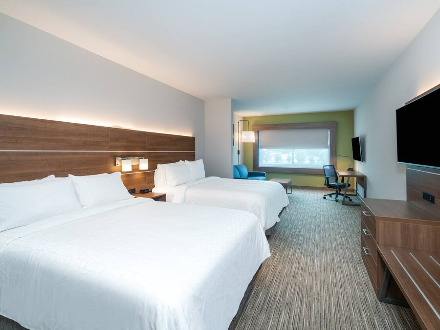 A hotel room with two beds, a desk with a chair, a TV, and a large window.