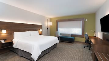 Quarto de hotel com uma cama grande, uma escrivaninha, uma cadeira, um pequeno sofá e uma televisão.