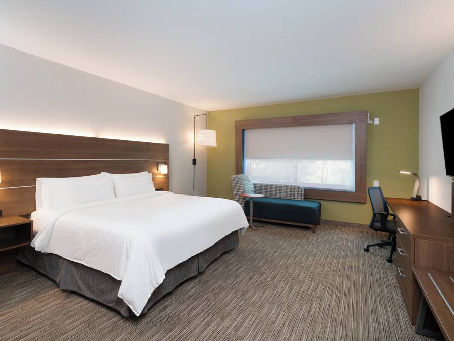 Quarto de hotel com uma cama grande, uma escrivaninha, uma cadeira, um pequeno sofá e uma televisão.