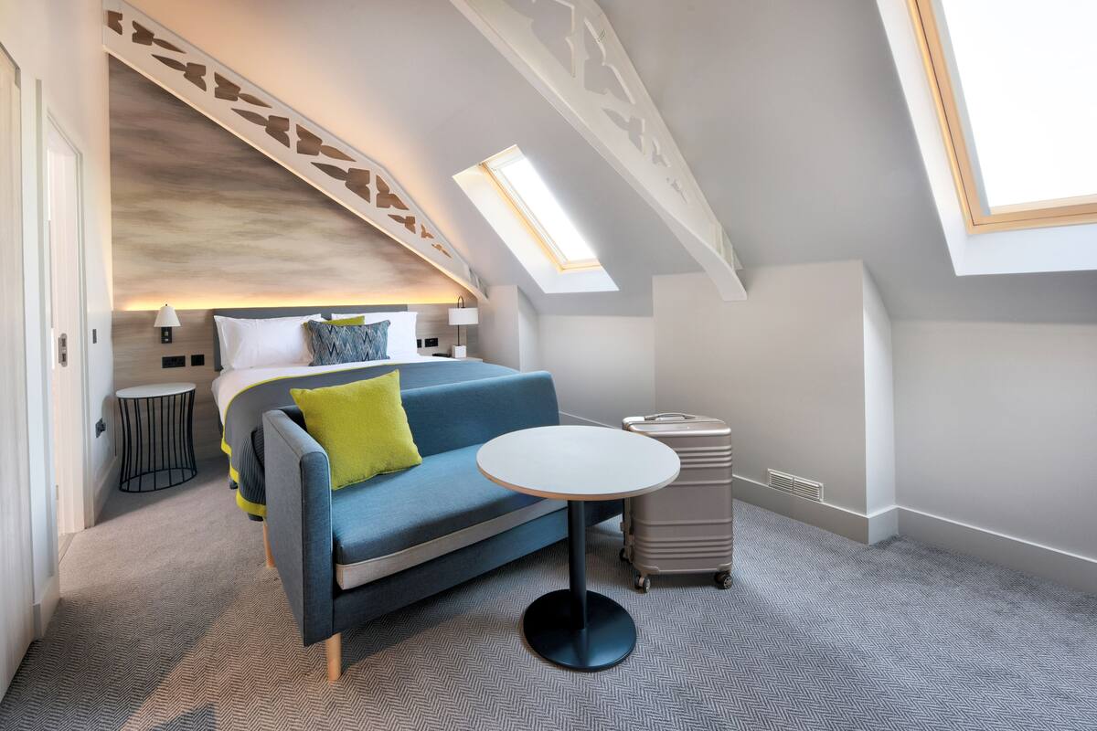 Un dormitorio moderno con cama, sofá azul, una mesita redonda y una maleta.