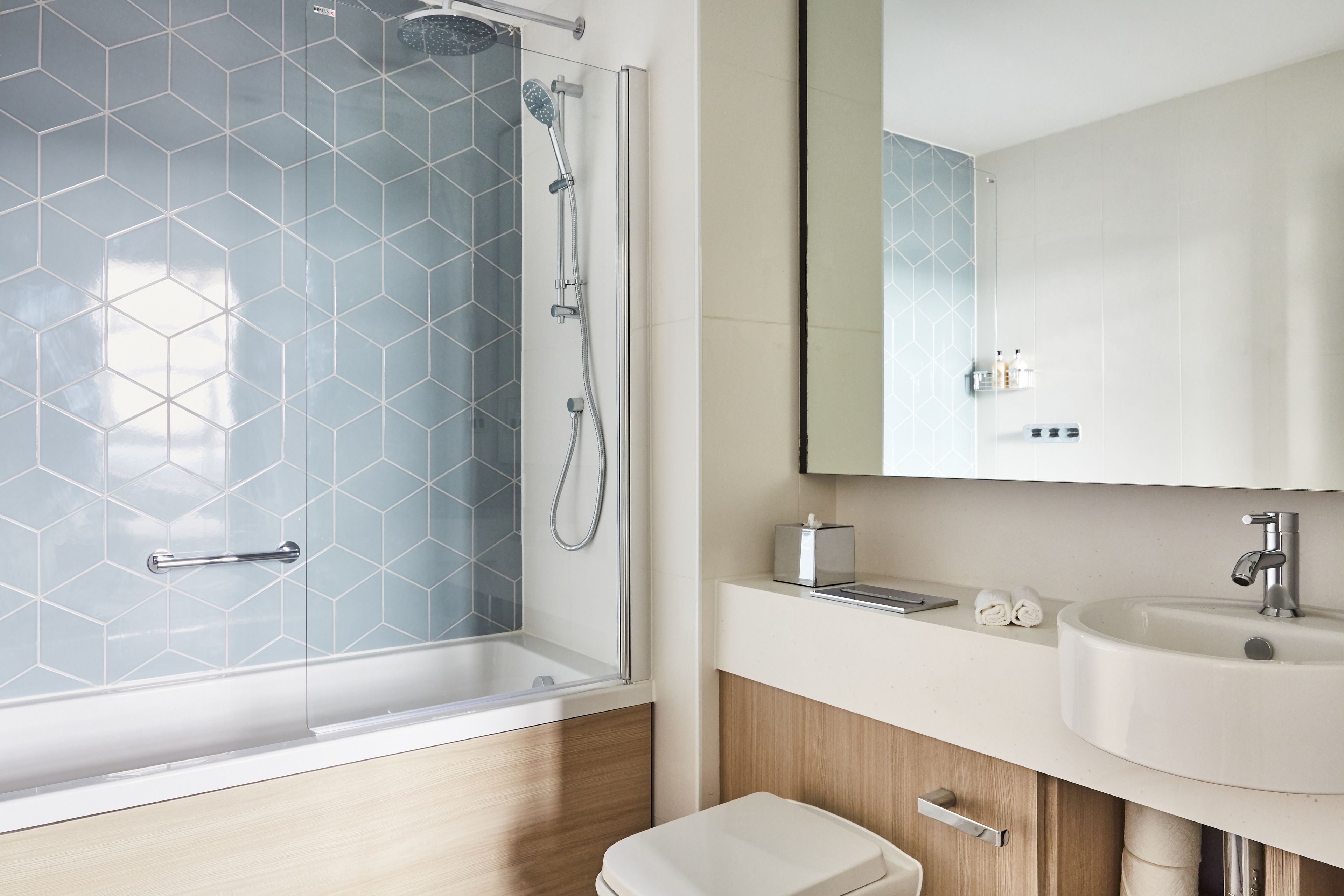 Un baño moderno con ducha envuelta en vidrio, un lavabo blanco y un armario de madera.