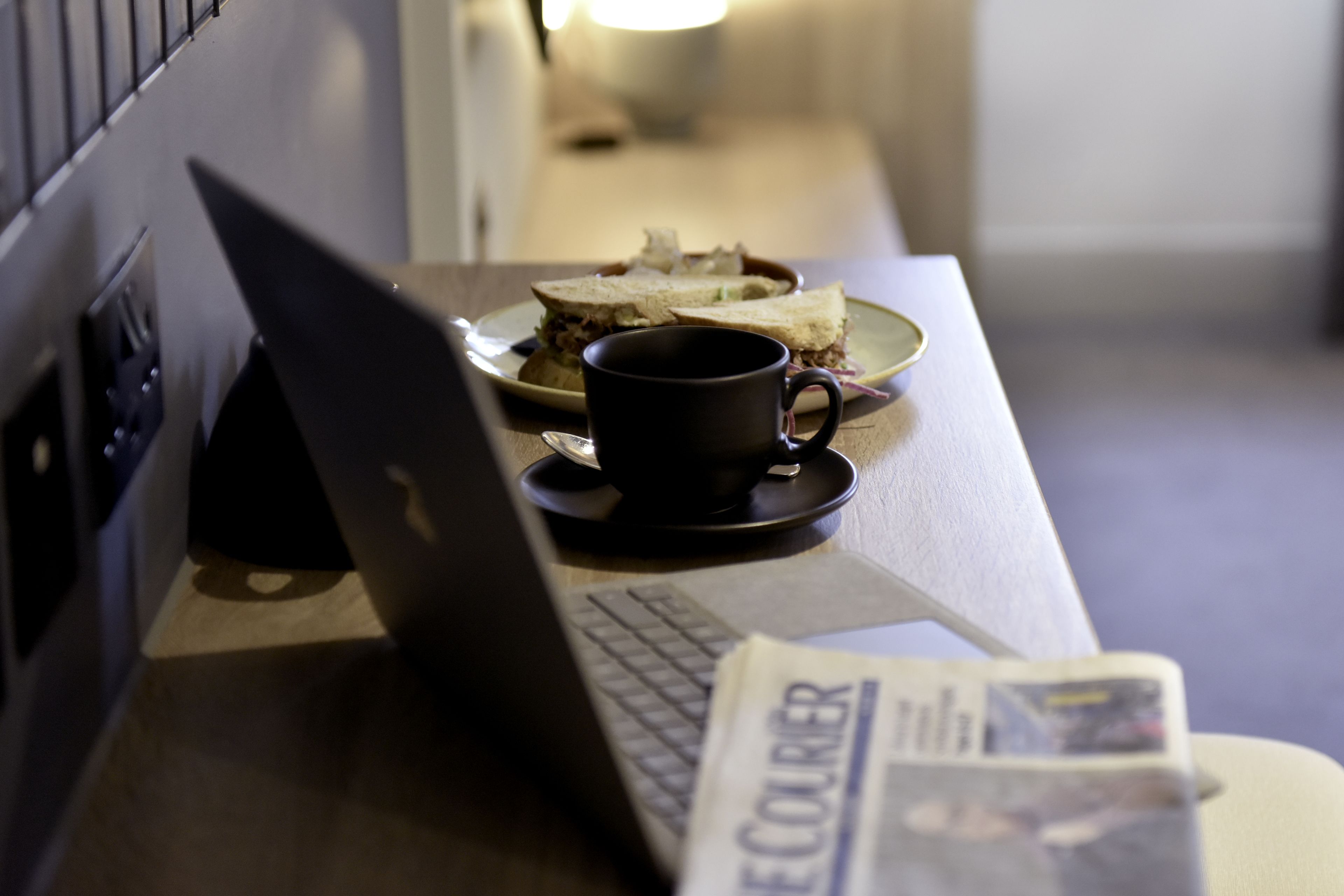 A laptop on a desk with a sandwich and a cup.