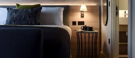 A hotel room with a bed, a bedside table with a lamp, and a view of a bathroom.