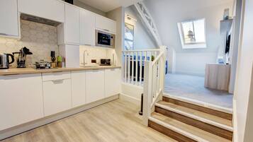 Une cuisine moderne avec des meubles blancs, un four à micro-ondes et un grille-pain. Un escalier mène à un balcon d’où l’on peut admirer un immeuble.