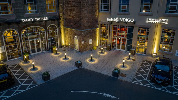 Een hotel binnenplaats met 'Daisy Taser' en 'Hotel Indigo' borden, een parkeerplaats en een 'Staybridge' gebouw.