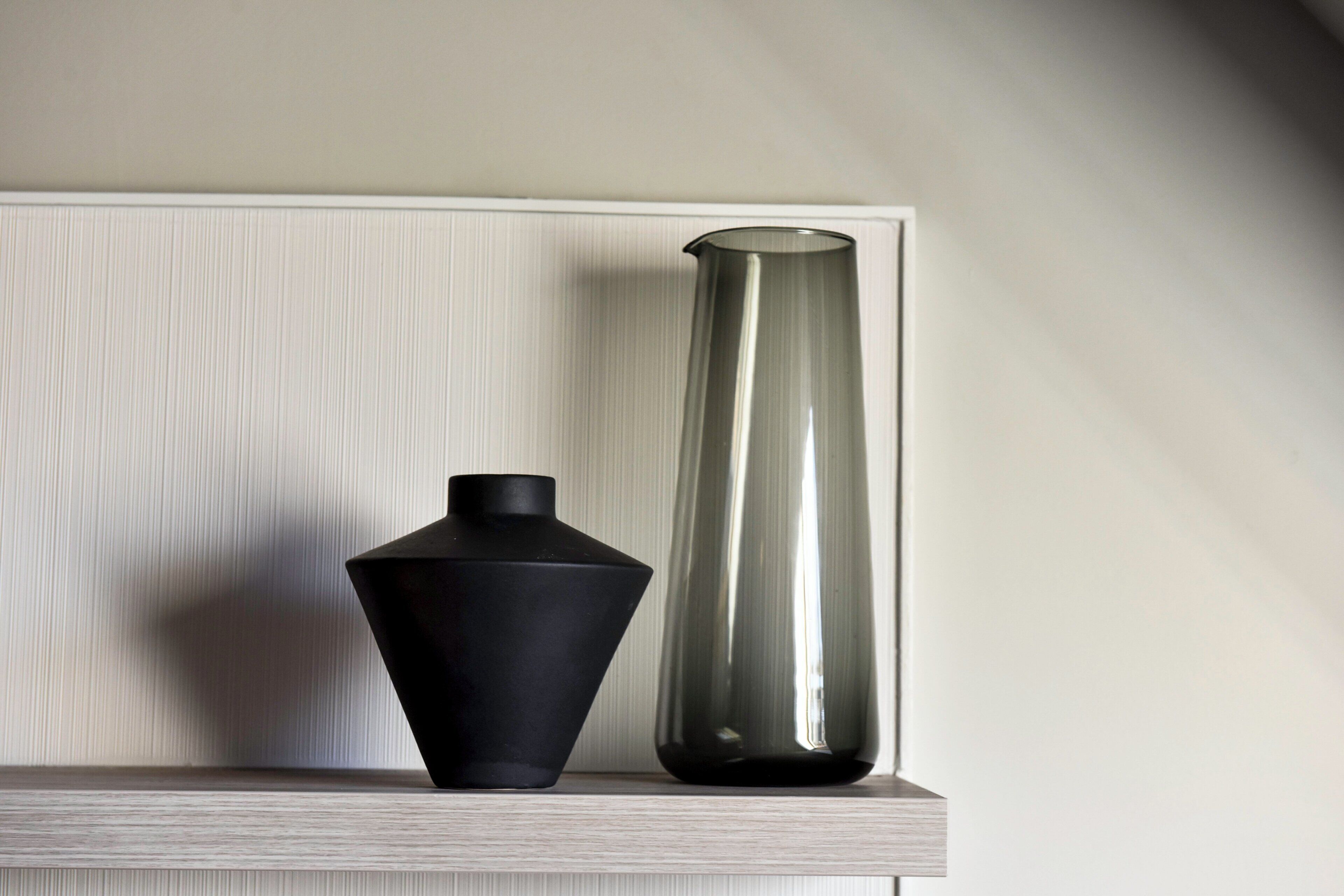 Two vases on a shelf against a wall.