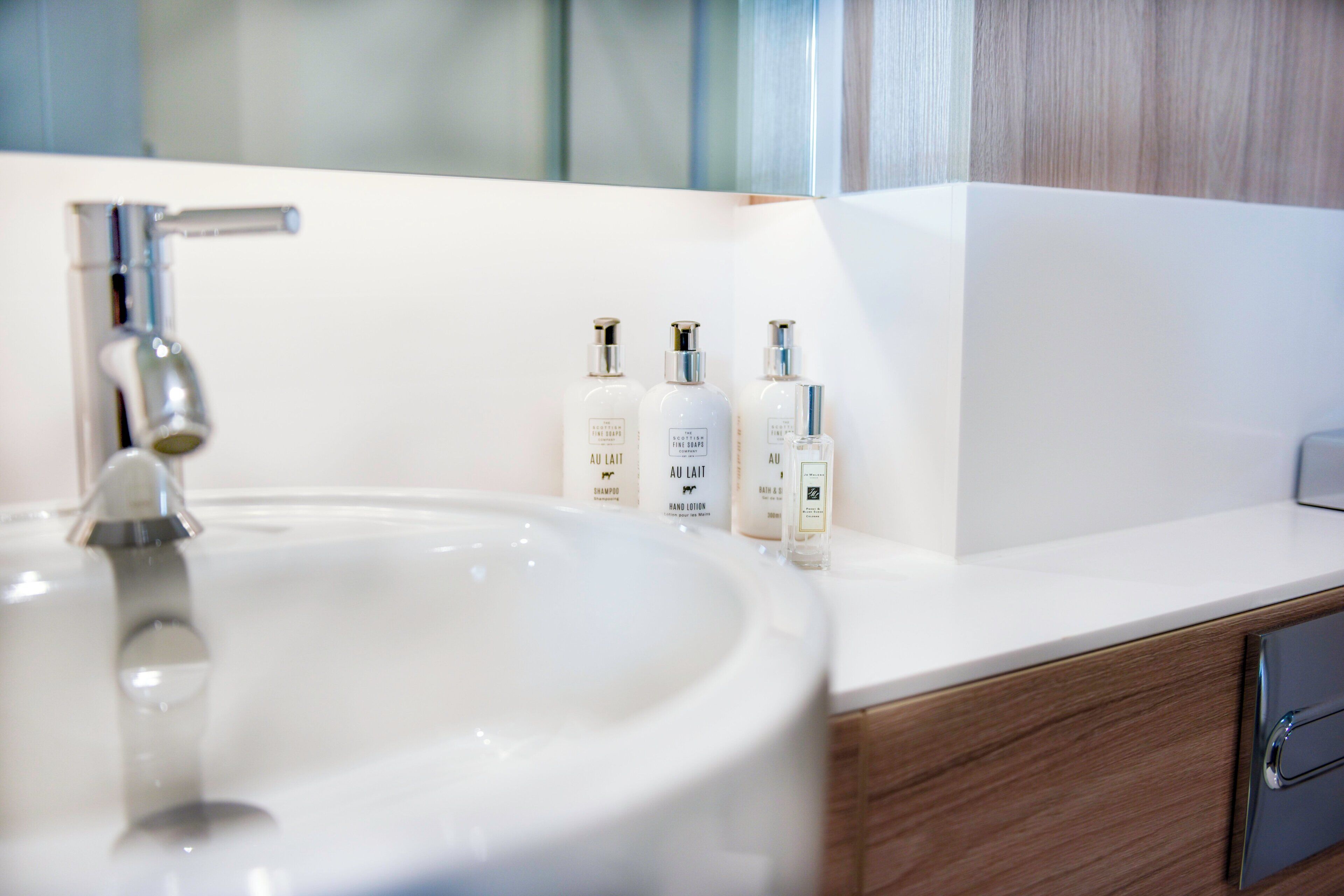 A bathroom with a white sink, a mirror, and three bottles of shampoo and lotion on the countertop.