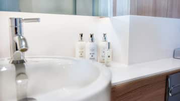 A bathroom with a white sink, a mirror, and three bottles of shampoo and lotion on the countertop.