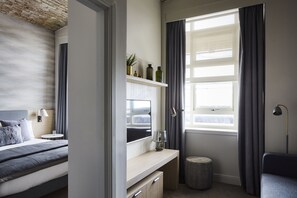 A modern hotel room with a bed, bedside table, TV, and a small round ottoman. - Staybridge Suites Dundee by IHG (Dundee)
