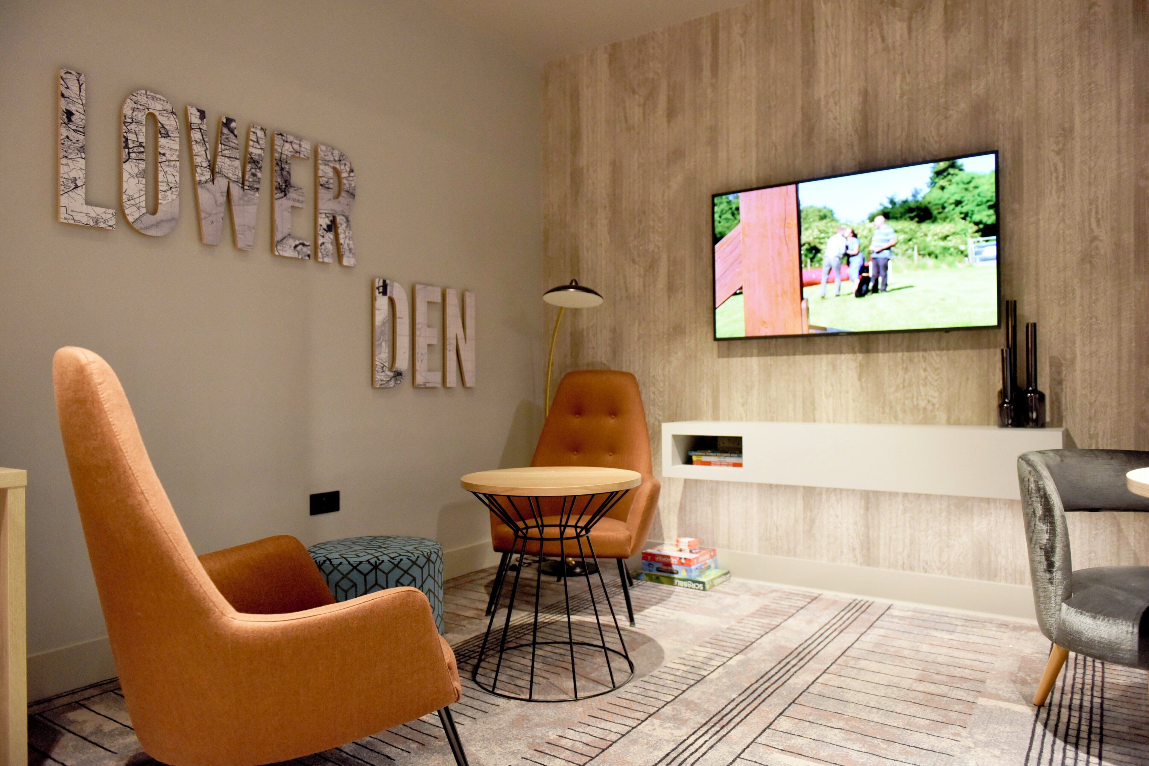 A modern living room with a television mounted on the wall, a round table, two chairs, and a patterned rug.